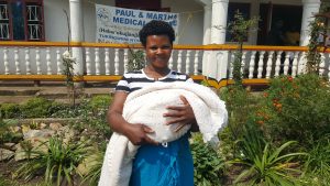 Una mujer con su bebe recien nacido de pie en frente de la clínica
